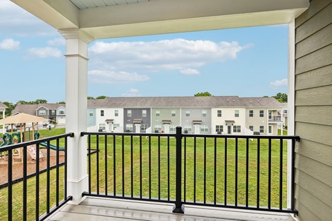 A balcony with a black railing overlooks a grassy area and buildings.