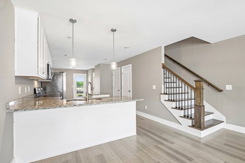 A modern kitchen with a marble countertop and a staircase with a wooden handrail.