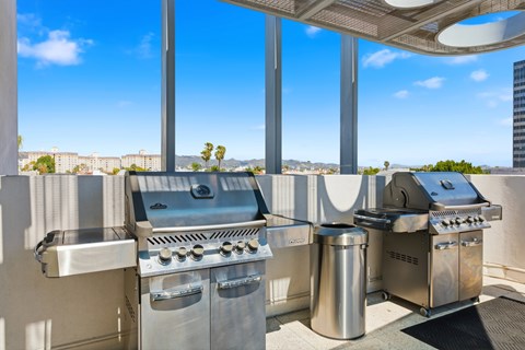 A set of outdoor grills on a balcony with a view of the city.