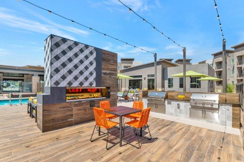 A wooden table with four orange chairs is in the foreground of an outdoor kitchen area.