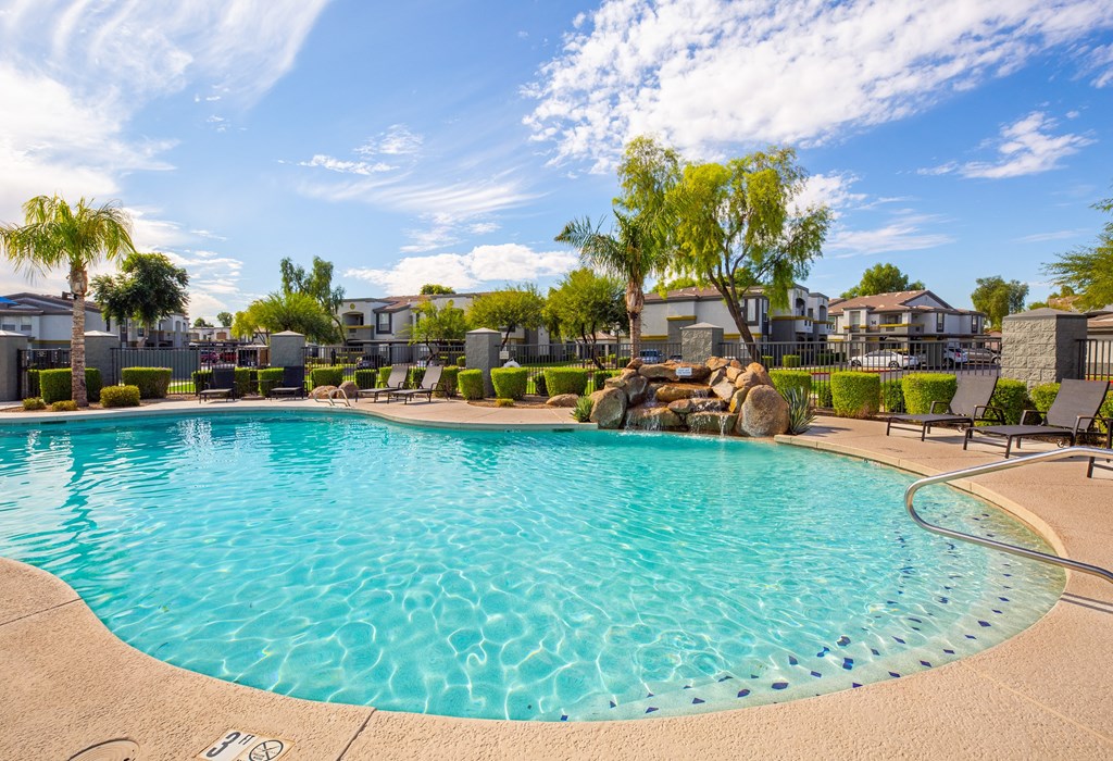 a resort style pool with a waterfall and trees in front of apartment buildings