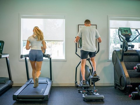 A man and a woman are exercising on treadmills in a gym.