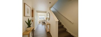 A hallway with a staircase and a mirror on the wall.