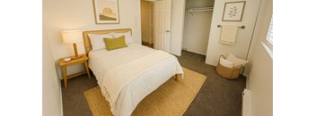 A bedroom with a bed, nightstand, and a basket on the floor.