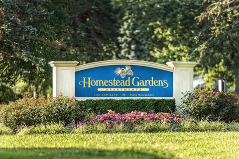 A sign for Homestead Gardens is displayed in front of some trees.