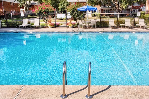 A pool with a blue umbrella and chairs in the background.