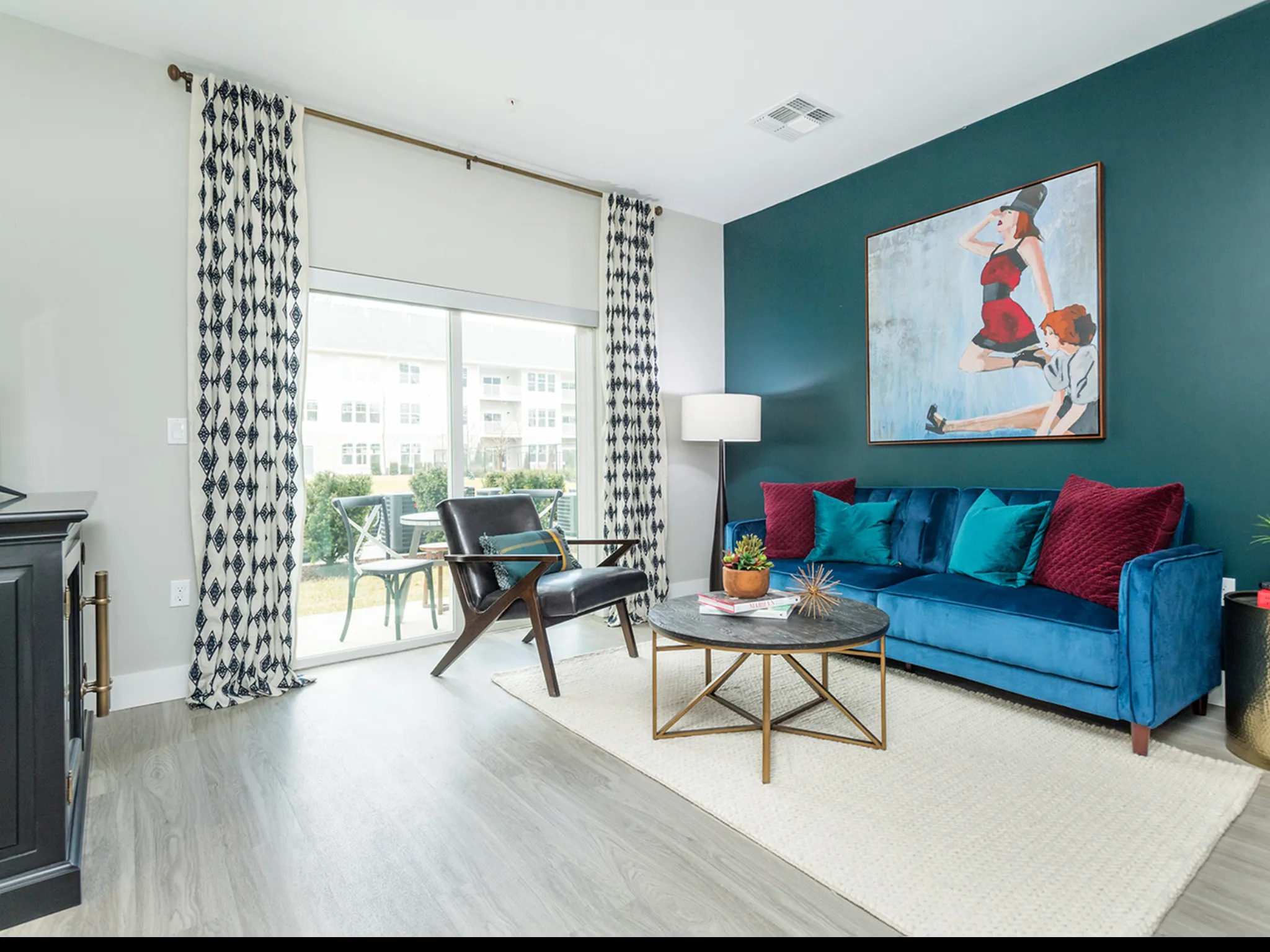 A living room with a blue couch, a wooden chair, a coffee table, and a painting on the wall.
