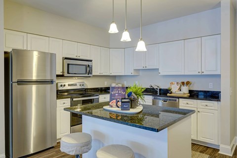 A kitchen with a refrigerator, microwave, and bar stools.