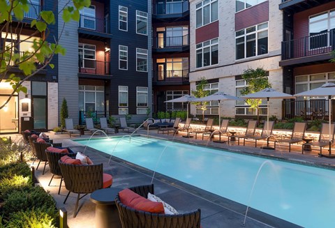 A pool surrounded by chairs and umbrellas in front of a building.