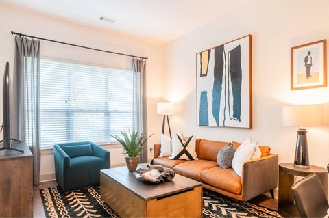 A living room with a brown couch, a blue chair, and a painting on the wall.