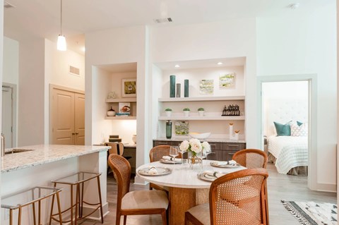A dining room with a table set for two and a kitchen area in the background.