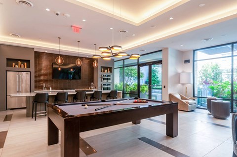 A pool table is in the middle of a room with a bar and a television.
