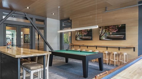 A pool table is in the middle of a room with a bar and a television.