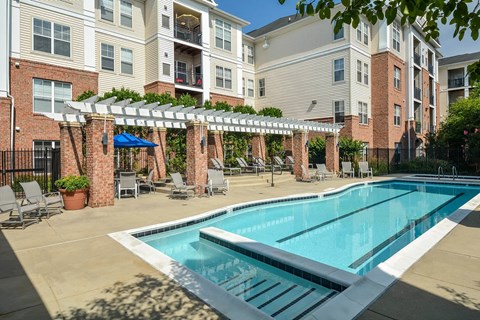 A swimming pool surrounded by a patio with chairs and a pergola.