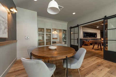 A modern dining room with a round wooden table and four grey chairs.