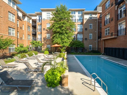 A pool surrounded by chairs and plants in front of apartment buildings.