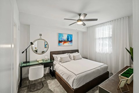 A bedroom with a bed, desk, chair, and a ceiling fan.