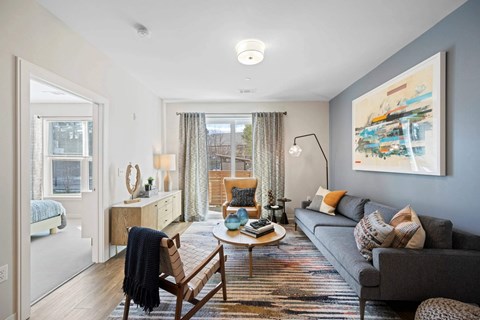 A living room with a grey couch, a wooden chair, and a painting on the wall.