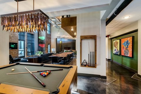 A pool table is in the middle of a room with a green wall and a painting hanging on it.