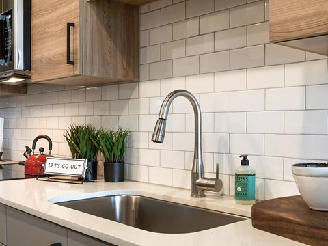 A kitchen sink with a faucet and a red kettle on the counter.