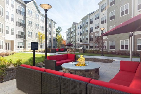 A patio with red couches and a fire pit in front of apartment buildings.
