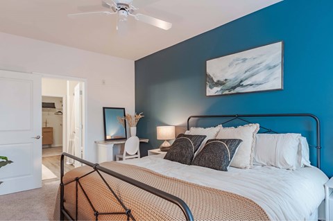 A bedroom with a bed, a ceiling fan, and a painting on the wall.