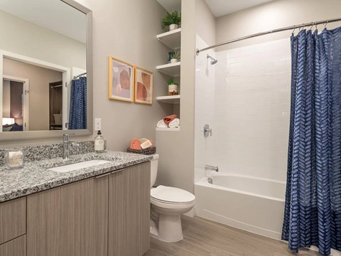 A bathroom with a white toilet, a sink with a marble countertop, a shower with a blue curtain, and a mirror above the sink.