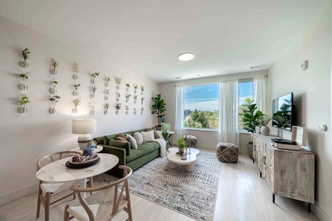 A living room with a green couch, a white table, and a TV on the wall.