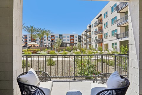 Two chairs are on a balcony with a view of apartment buildings.