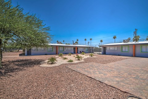 A sunny day at a gravel courtyard with a building and palm trees in the background.