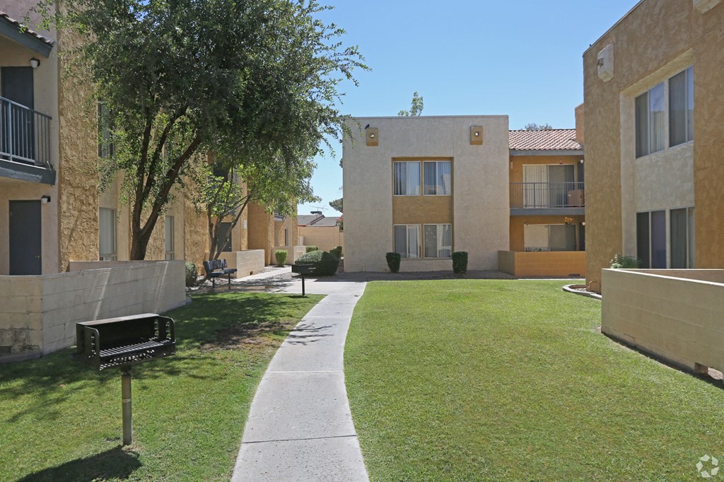 a walkway between two apartment buildings with a lawn and a tree