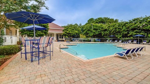 A pool area with a blue umbrella and chairs.