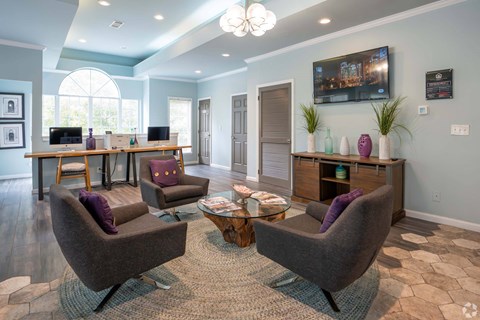 A living room with a large window, a desk, and a TV mounted on the wall.