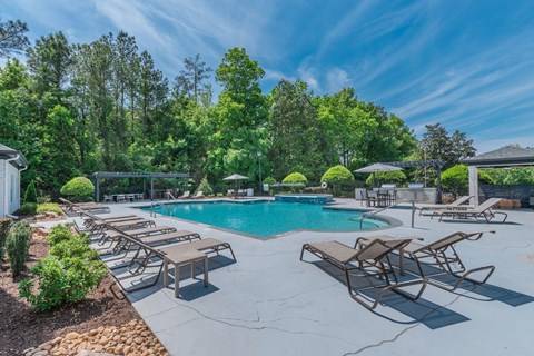 A pool surrounded by trees and lounge chairs.