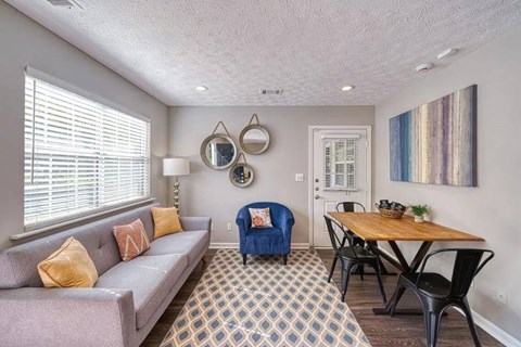 A living room with a grey couch, a blue chair, a wooden table, and a patterned carpet.