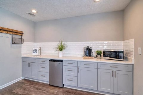 A kitchen with a white subway tile backsplash and grey cabinets.
