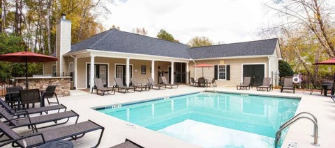 A pool in front of a house with a black umbrella.