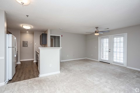 A spacious living room with a ceiling fan and a kitchen area with a refrigerator and a microwave.