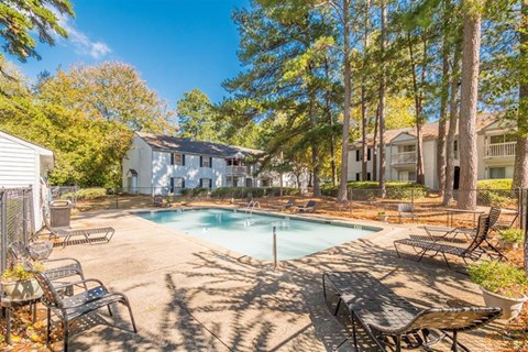A pool surrounded by trees and chairs in a sunny backyard.