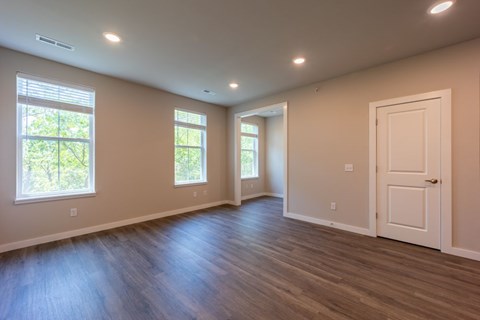 A room with a white door and two windows with a view of trees.
