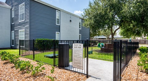 A sign in front of a fence reads "ENJOY THE BARK PARK".