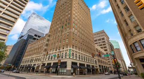 A tall building with a green sign on the front is in the middle of a city street.
