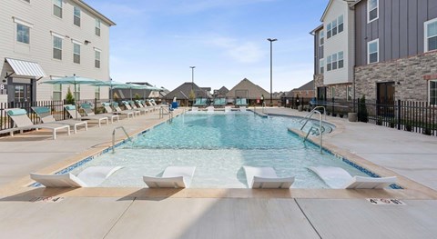 A large outdoor swimming pool with lounge chairs and a fence.