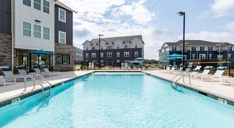 A large swimming pool in front of a building with lounge chairs around it.
