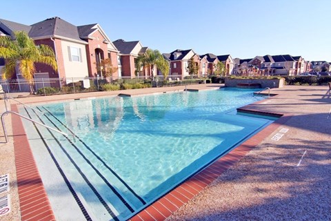 A swimming pool surrounded by a brick border with a residential area in the background.