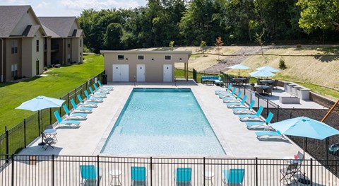 A large outdoor swimming pool surrounded by a black fence and blue lounge chairs.