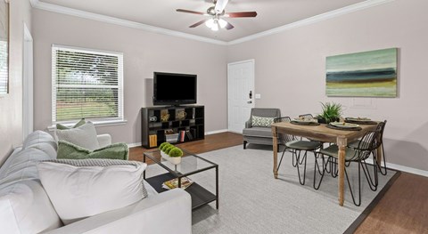 A living room with a white couch, a coffee table, a dining table, and a painting on the wall.
