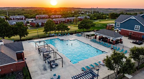 A sunset view of a pool area with lounge chairs and a fence.