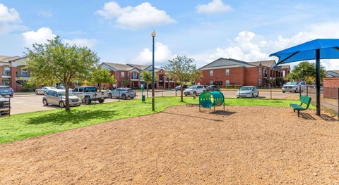 A playground area with a blue umbrella and a green bench.