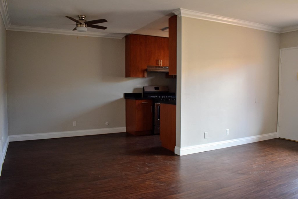 an empty living room with a kitchen and a ceiling fan